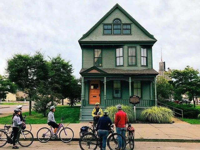 Radfahrer versammelt vor einem grünen, zweistöckigen historischen Haus.