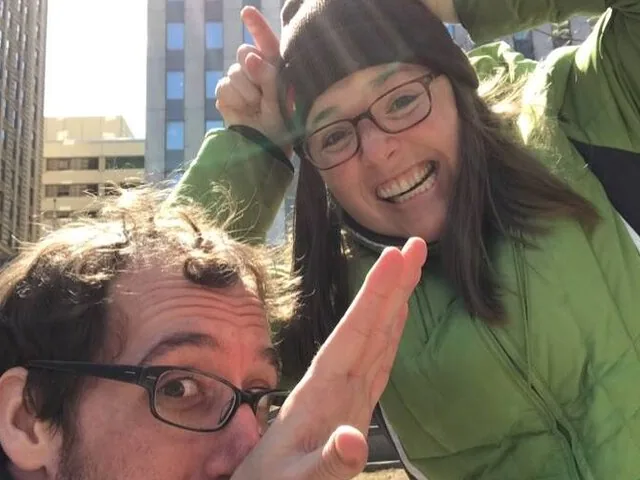 A close-up selfie of a man and woman making funny faces outdoors.