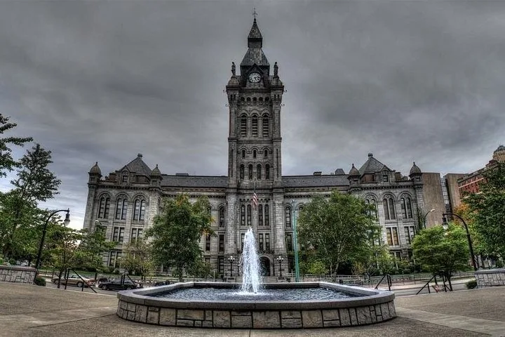 Großes Steingebäude mit einem Uhrenturm und einem Brunnen