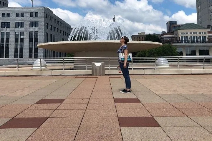 Frau blickt auf einem städtischen Platz zu einem Brunnen hinauf
