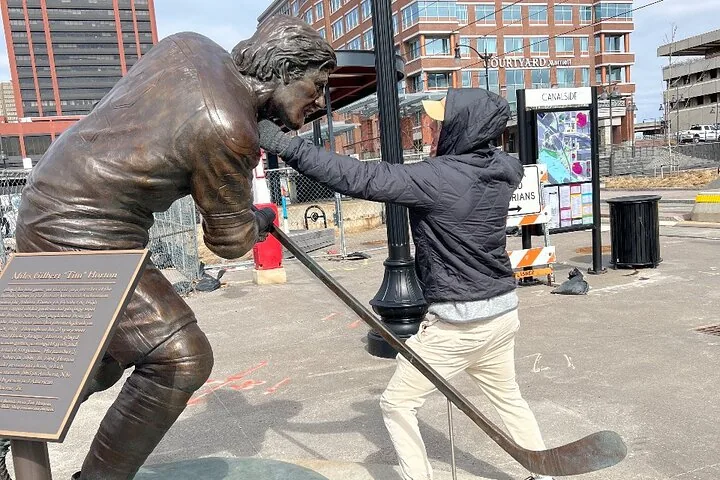 A man pretending to punch a bronze statue of a hockey player