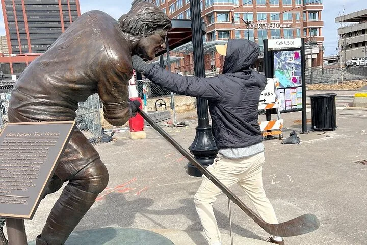 Ein Mann schlägt spielerisch auf eine Bronzestatue eines Eishockeyspielers in Buffalo
